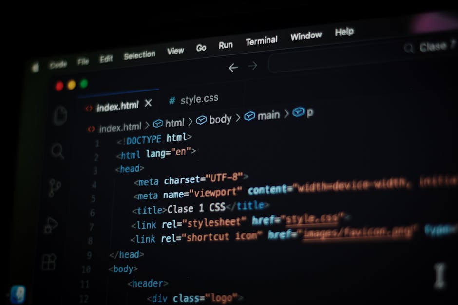 A person’s hands are visible typing on a closed laptop with a dark, sleek exterior. The screen displays a coding interface with multicolored lines of code, primarily in green, blue, and white, set a